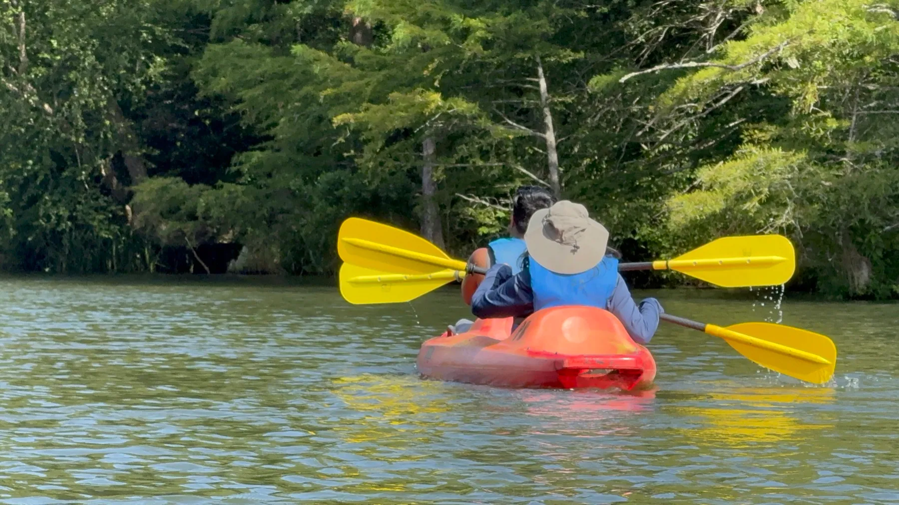 Two people in a tandem kayak with both paddles raised at the same angle